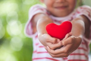 Cute asian little child girl showing and holding red heart in hand with care and love